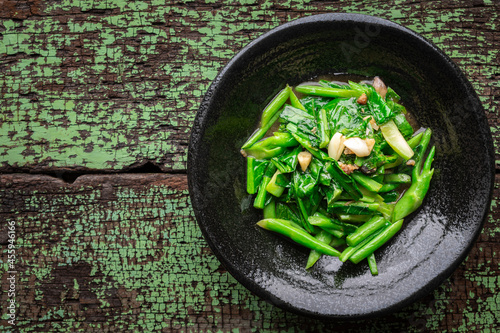 stir fried collards with salted fish and garlic in black ceramic plate on green old wood texture background with copy space for text, top view, collard greens photo