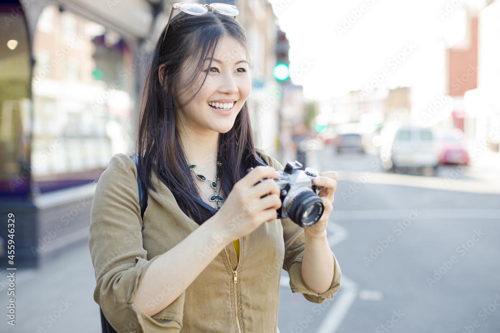 Smiling young female tourist photographing with camera on urban street