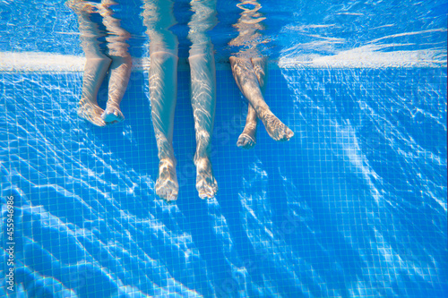 4 pairs of feet under water in a swimming pool