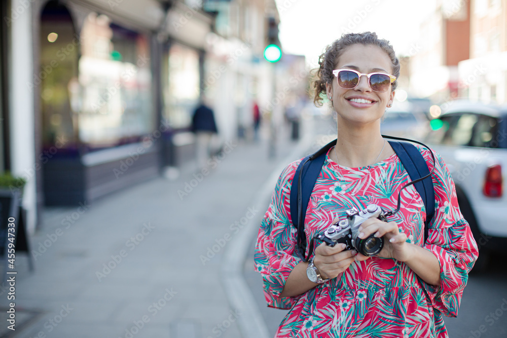 Fototapeta premium Portrait laughing, enthusiastic young female tourist in sunglasses photographing with camera on urban street