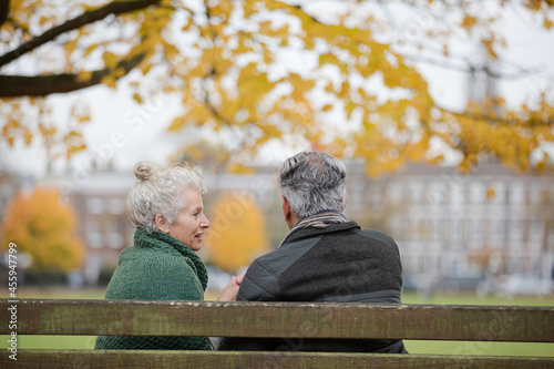 Affectionate senior couple talking on bench in autumn park