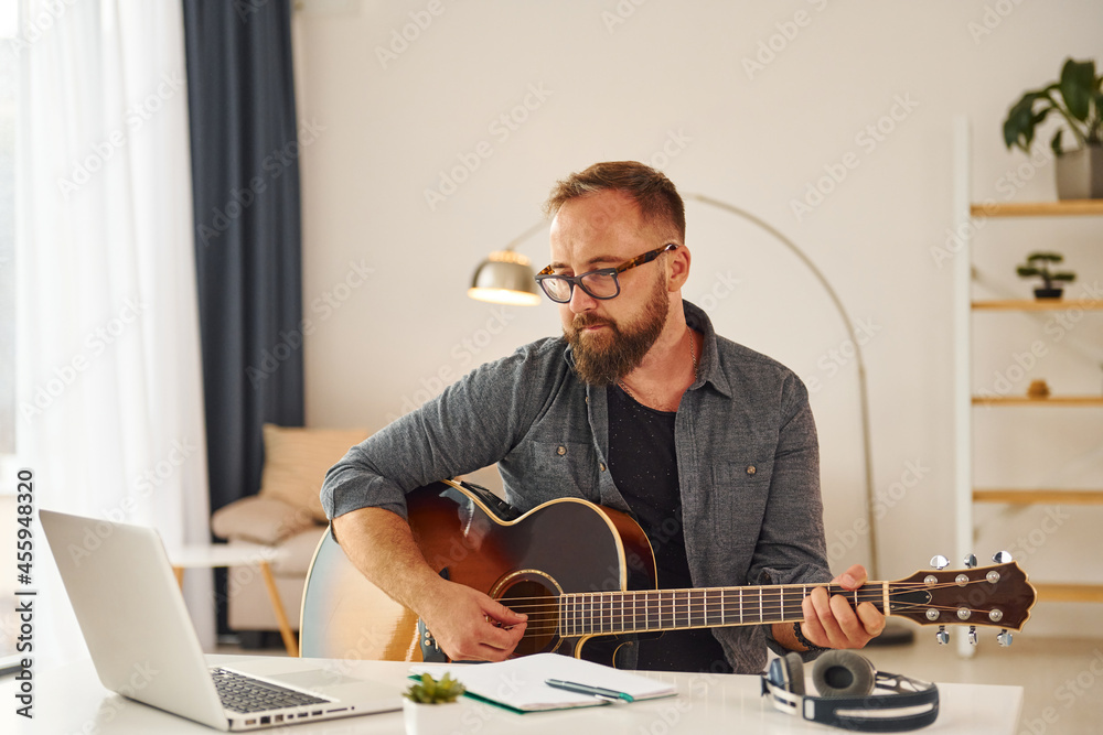 Writing some ideas. Man in casual clothes and with acoustic guitar is indoors Writing some ideas. Man in casual clothes and with acoustic guitar is indoors
