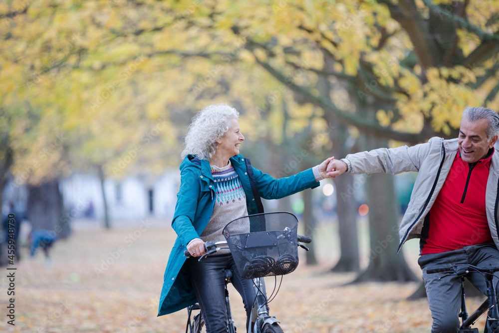 Obraz premium Senior couple bike riding among trees and leaves in autumn park