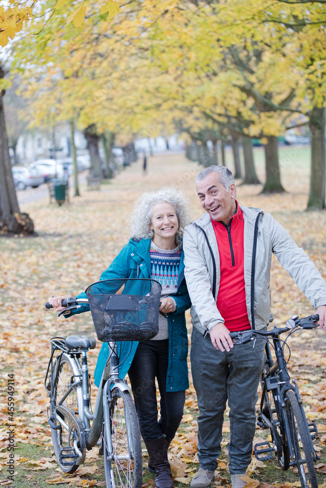 Senior couple walking bicycles among trees and leaves in autumn park