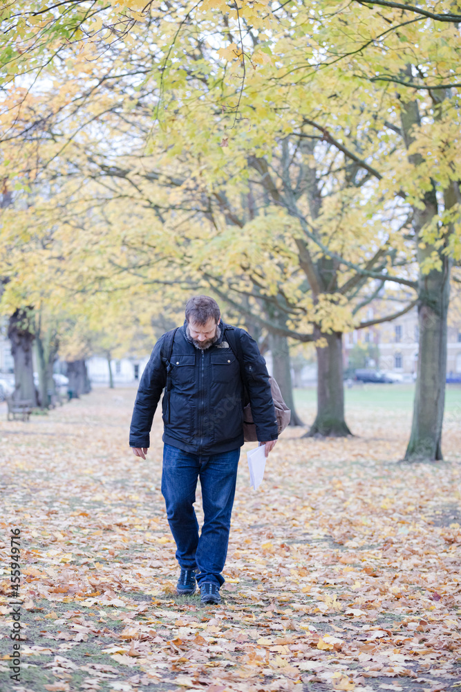 Fototapeta premium Senior man walking among leaves in autumn park