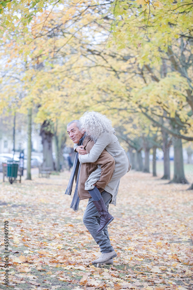 Fototapeta premium Senior man carrying woman on his back in autumn park