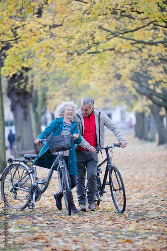 Fototapeta Naklejka Na Ścianę i Meble -  Senior couple walking bicycles among trees and leaves in autumn park