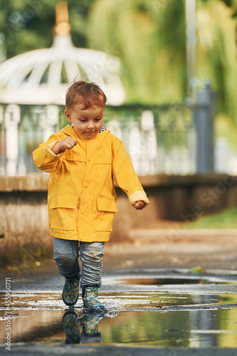 Little boy in yellow coat have a walk outdoors in the park after the rain