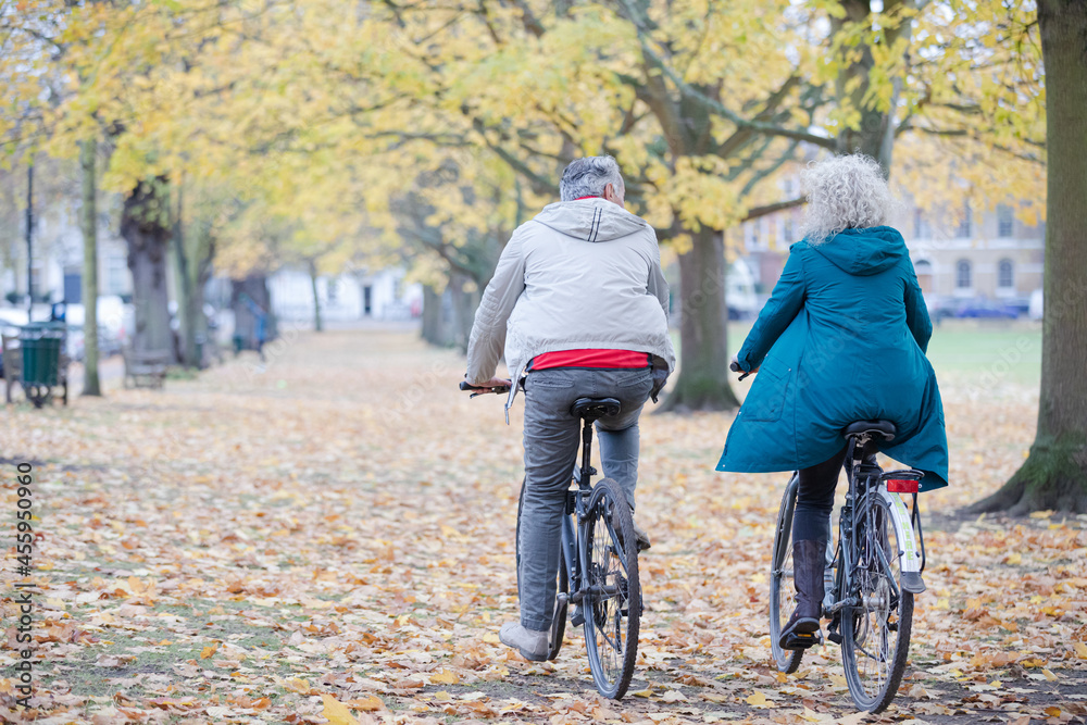 Senior couple bike riding among trees and leaves in autumn park