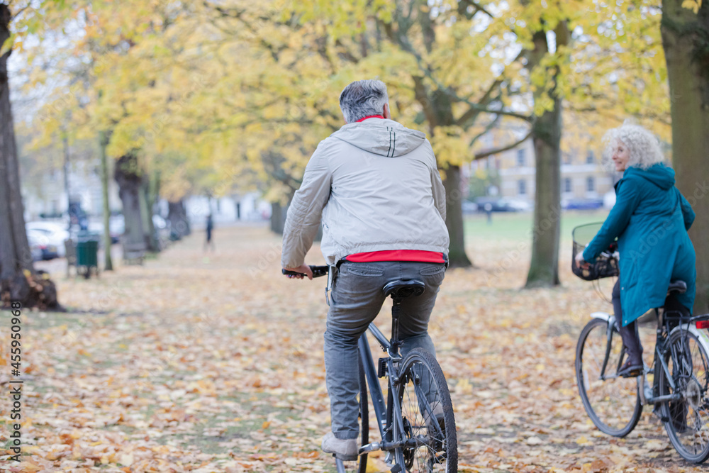 Obraz premium Senior couple bike riding among leaves and trees in autumn park