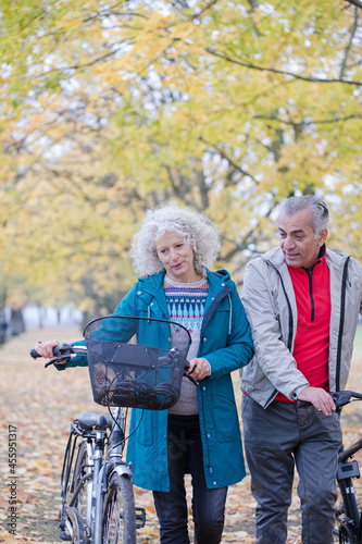 Senior couple walking bicycles among trees and leaves in autumn park