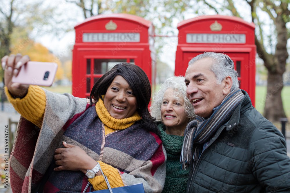 Senior friends taking selfie in front of red telephone booths in autumn park