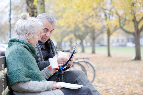 Senior couple reading newspaper and drinking coffee on bench in autumn park © KOTO