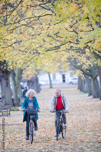 Senior couple bike riding among trees and leaves in autumn park