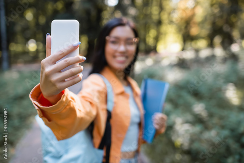 blurred asian woman taking selfie on mobile phone in park © LIGHTFIELD STUDIOS