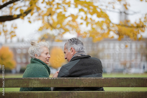 Affectionate senior couple sitting on bench in autumn park