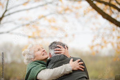 Smiling, affectionate senior couple hugging on bench in autumn park