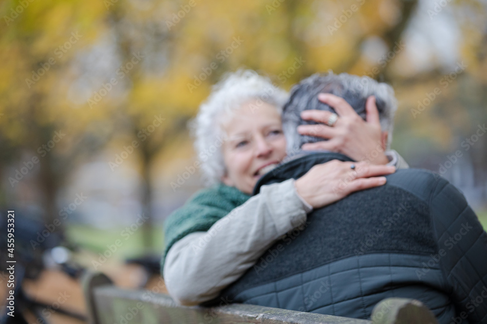 Smiling, affectionate senior couple hugging on bench in autumn park Smiling, affectionate senior couple hugging on bench in autumn park