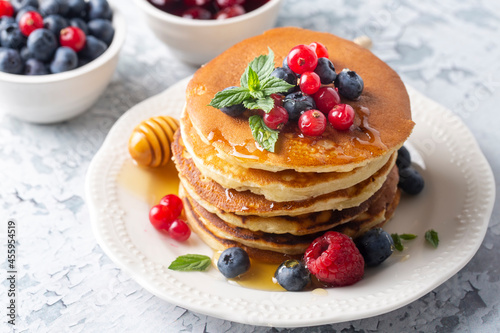 Healthy summer breakfast, homemade classic american pancakes with fresh fruit and honey, morning light gray stone background copy space top view
