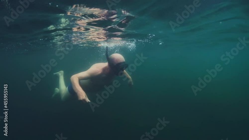 First time snorkeling. Elderly man carefully swims in the lake with mask for the first time in his life and explores underwater world. Active senior man snorkeling in the freshwater lake photo