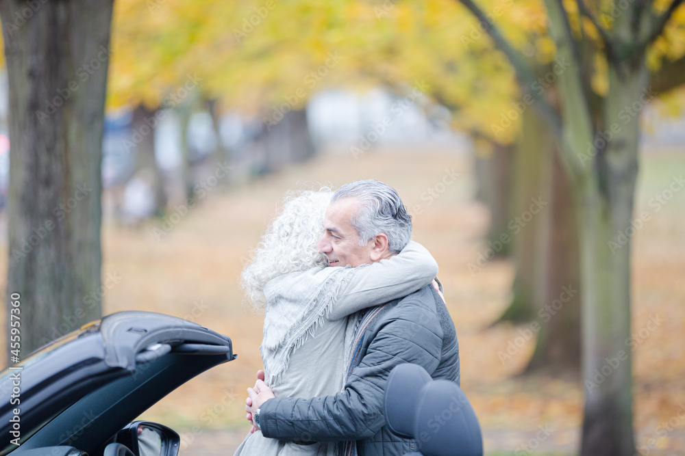 Fototapeta premium Affectionate, tender senior couple hugging in autumn park near car