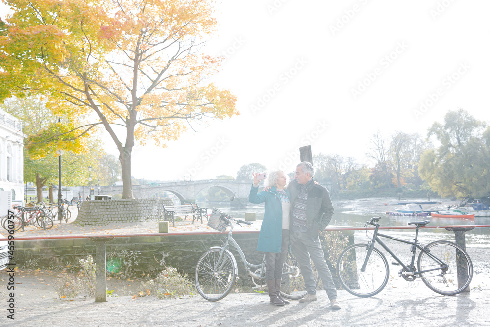 Obraz premium Senior couple with bicycles taking selfie at autumn river