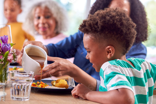 Mother Pouring Gravy Onto Son's Meal As Multi Generation Family Sit Around Table At Home photo