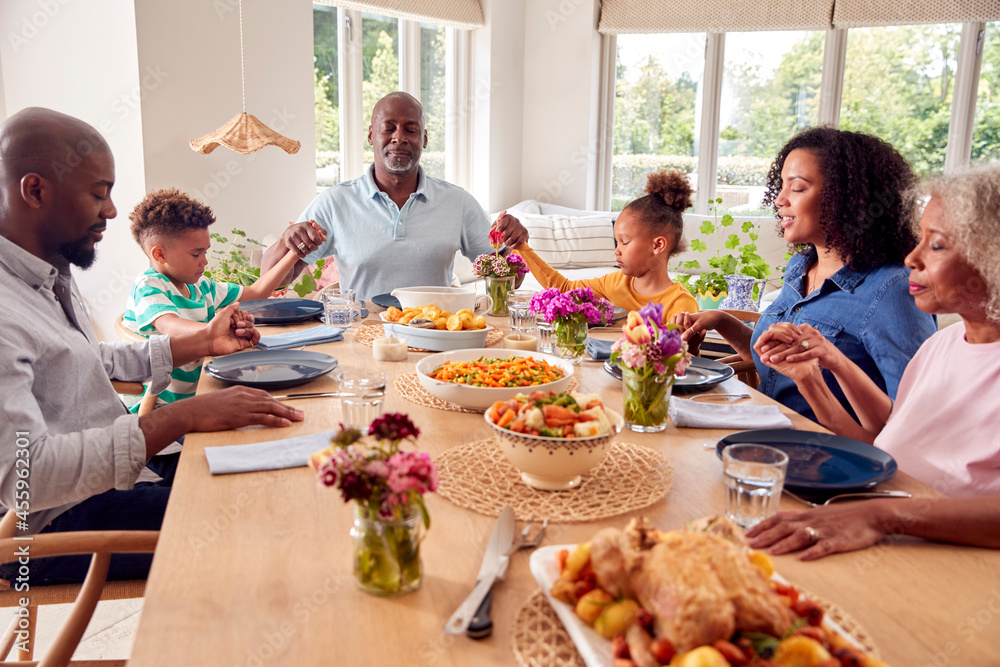 Multi Generation Family Holding Hands Around Table At Home Saying Grace Before Eating Meal Together