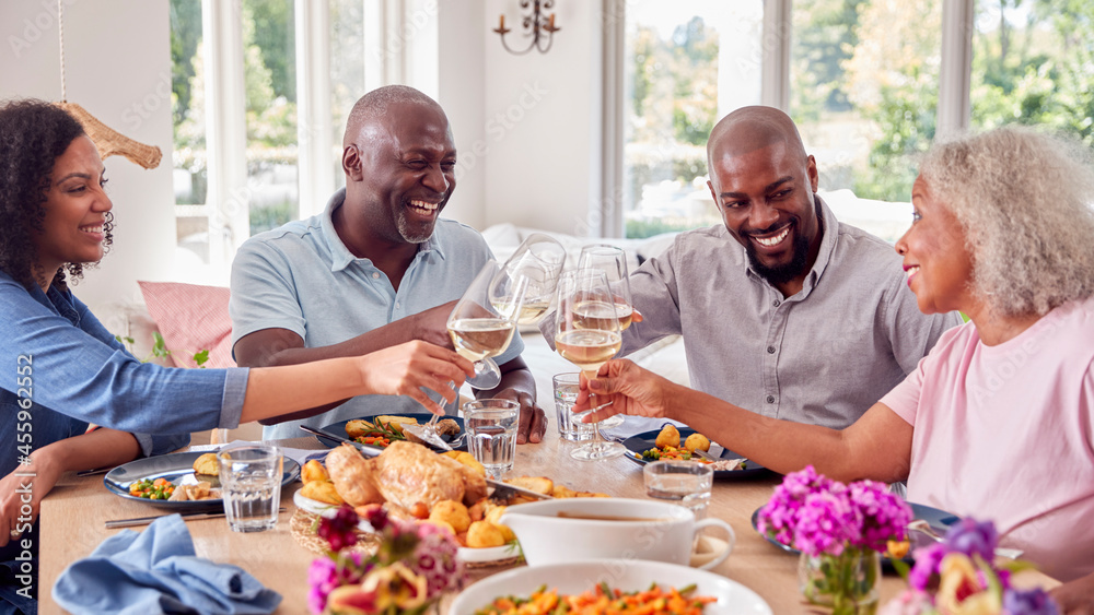 Senior Parents With Adult Offspring Making Toast Sitting Around Table For Family Meal Senior Parents With Adult Offspring Making Toast Sitting Around Table For Family Meal