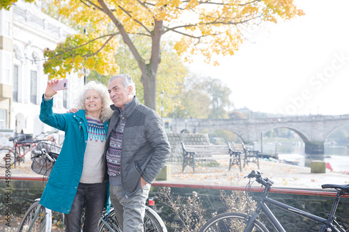 Senior couple with bicycles taking selfie at autumn river