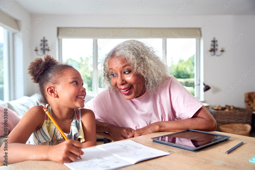Fototapeta premium Grandmother Helping Granddaughter With Home Schooling Sitting At Table With Digital Tablet