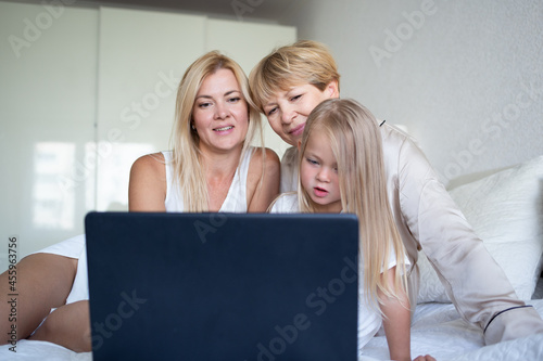 little girl with mom and grandmother are sitting on the bed in front of a laptop