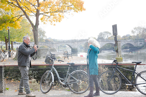 Senior man photographing wife with bicycle in autumn city