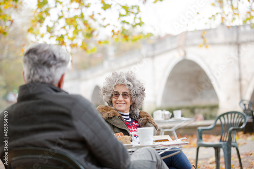 Active senior couple talking, enjoying coffee at autumn park cafe