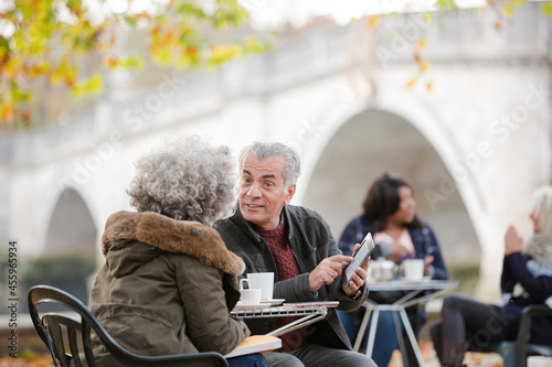 Senior couple using digital tablet, enjoying coffee and tea at autumn park