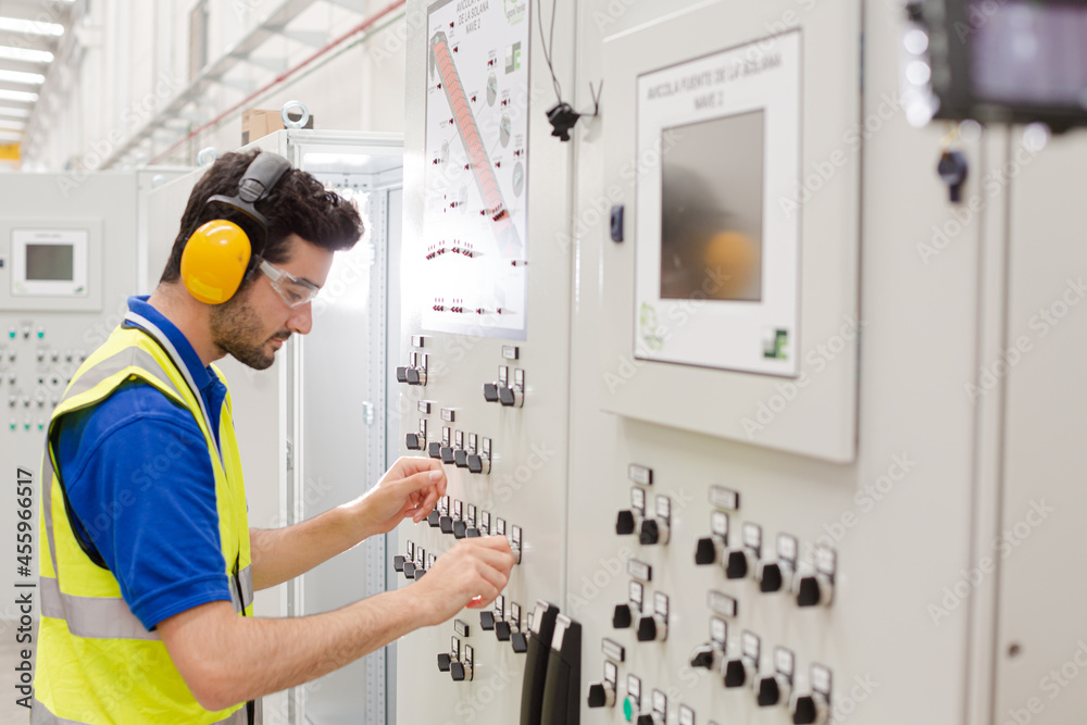 Male worker wearing ear protectors, operating machinery at control panel in factory Male worker wearing ear protectors, operating machinery at control panel in factory