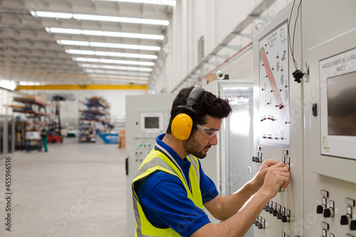 Male worker wearing ear protectors, operating machinery at control panel in factory photo