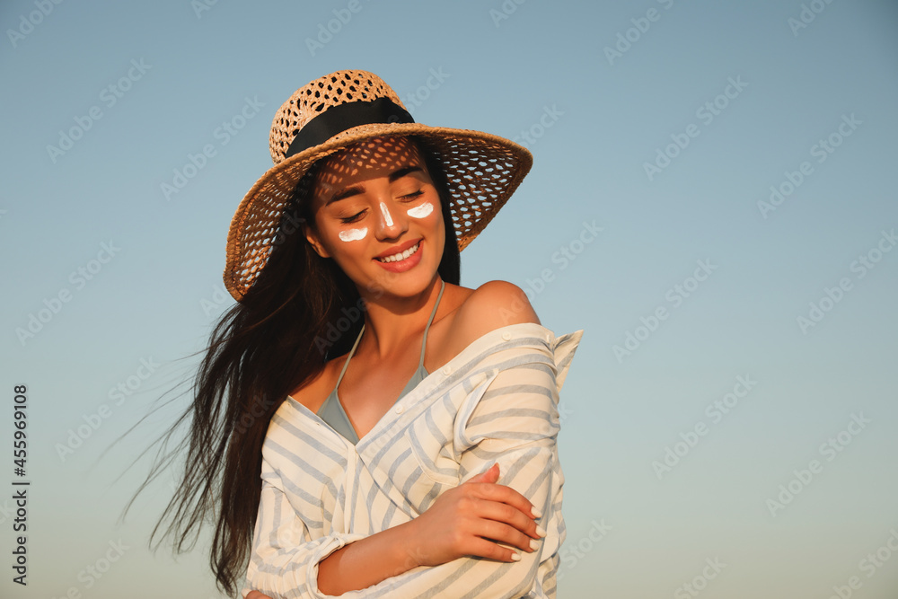 Happy young woman with sun protection cream on face against blue sky