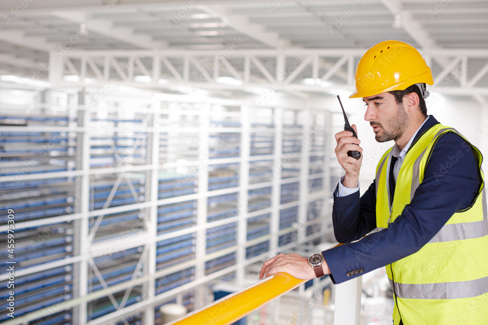 Male supervisor using walkie-talkie on platform in factory Male supervisor using walkie-talkie on platform in factory