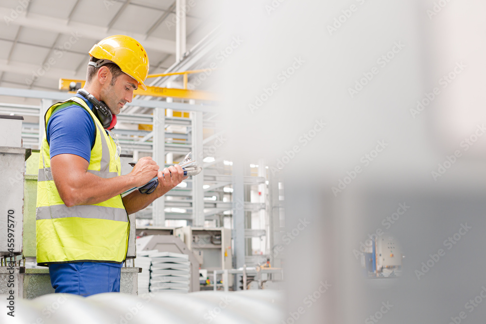 Factory worker with clipboard inspecting steel parts in factory Factory worker with clipboard inspecting steel parts in factory