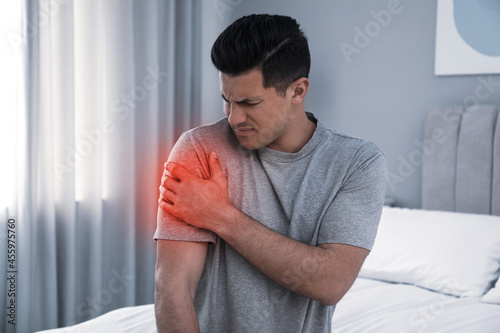 Man suffering from shoulder pain on bed at home photo