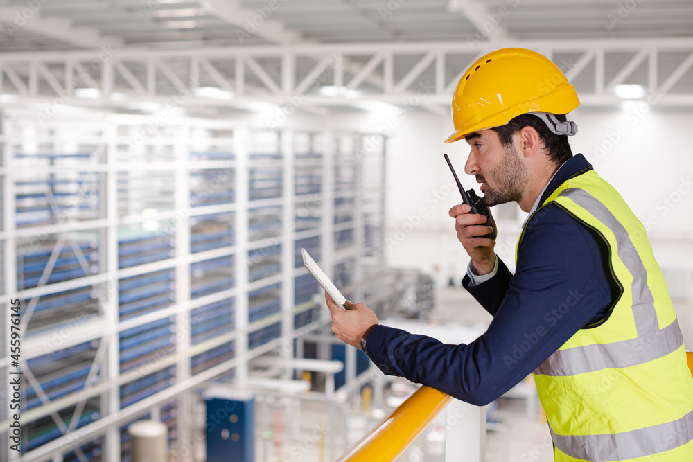 Male supervisor with digital tablet talking, using walkie-talkie on platform in factory Male supervisor with digital tablet talking, using walkie-talkie on platform in factory