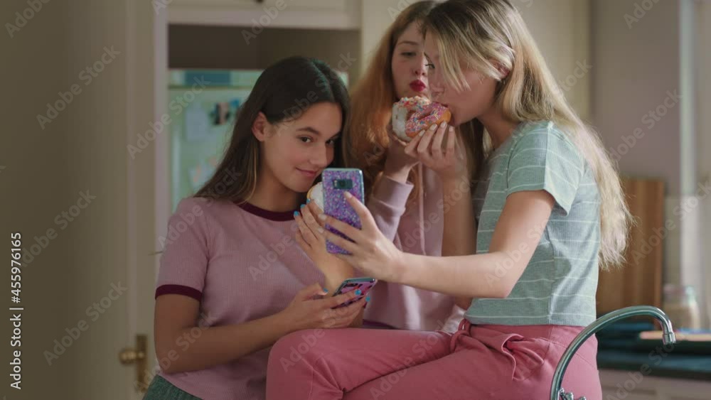 funny teenage girls posing with donuts taking photos using smartphone sharing on social media enjoying hanging out on weekend in kitchen