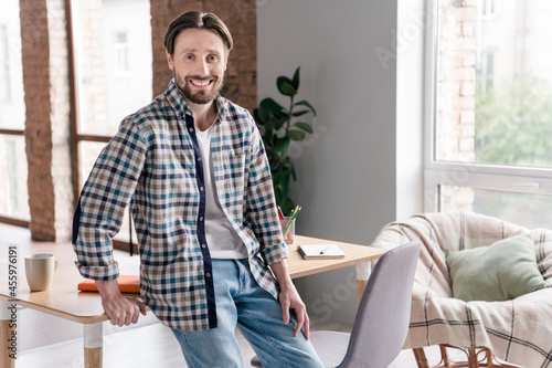 Photo of pretty adorable young man wear plaid shirt sitting table smiling indoors house office