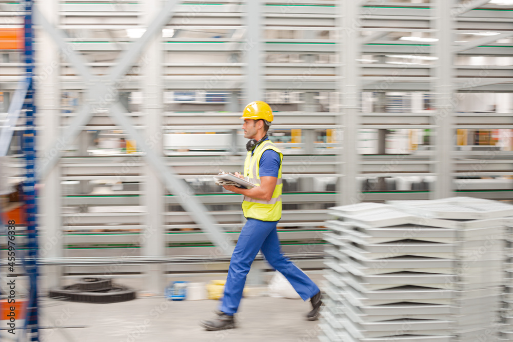 Factory worker with clipboard inspecting steel parts in factory Factory worker with clipboard inspecting steel parts in factory