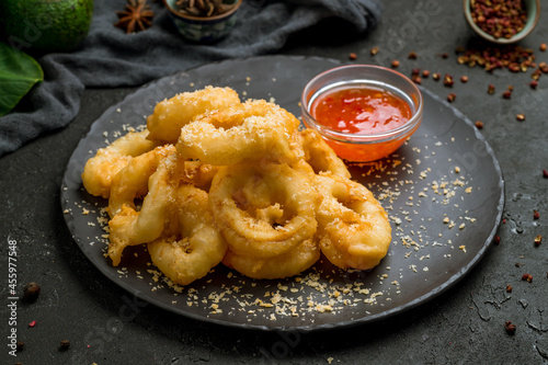 Rings of squid fried in a batter with sweet and sour sauce on dark stone table photo