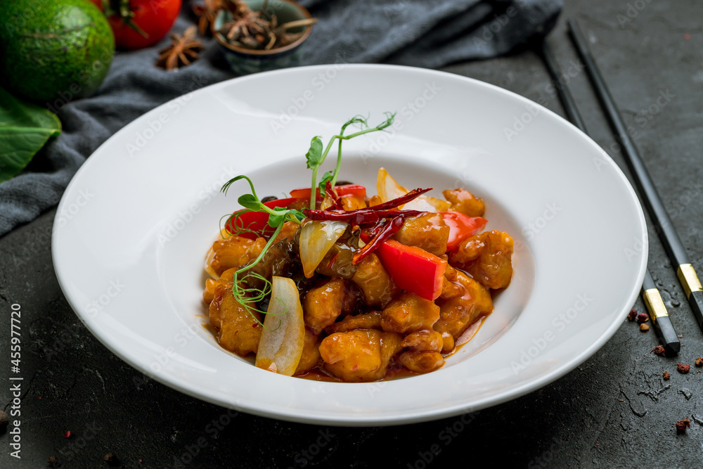 Sichuan fried chicken in sauce on white plate on dark stone table