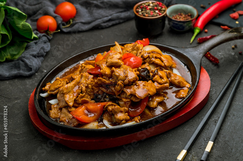 roast pork with vegetables in Chinese sauce in a hot frying pan on dark stone table
