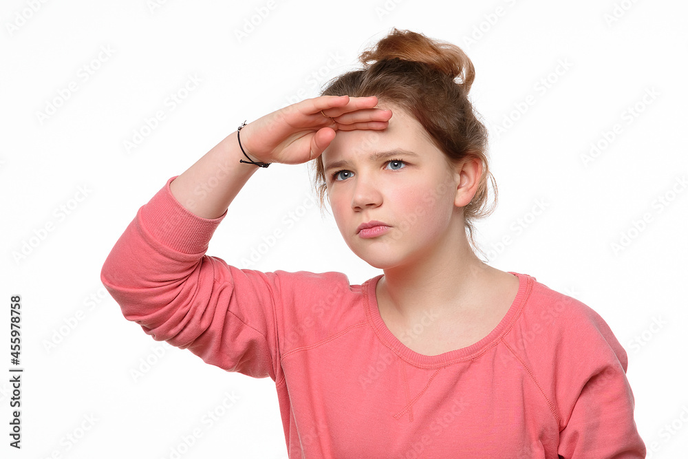 Portrait of a curious young girl looking far away with hand at her forehead, trying to see something far away