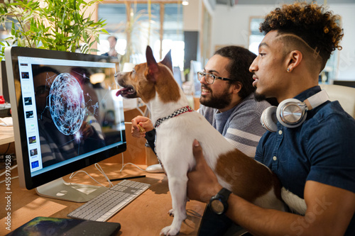 Man holding dog, sitting at computer with colleague photo